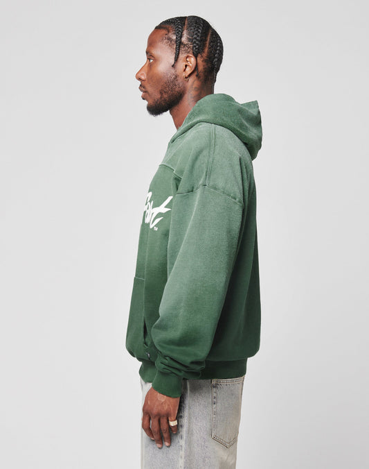 A man with braided hair wears an oversized LFDY Script Hooded by LIVE FAST DIE YOUNG in green and light-wash jeans, standing in profile against a plain white background.