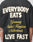 A person wears the LIVE FAST DIE YOUNG Everybody Eats Tee in black with bold yellow EVERYBODY EAT$ text. Only the back and arms are visible. Made from 100% Baumwolle (cotton) with easy care instructions.