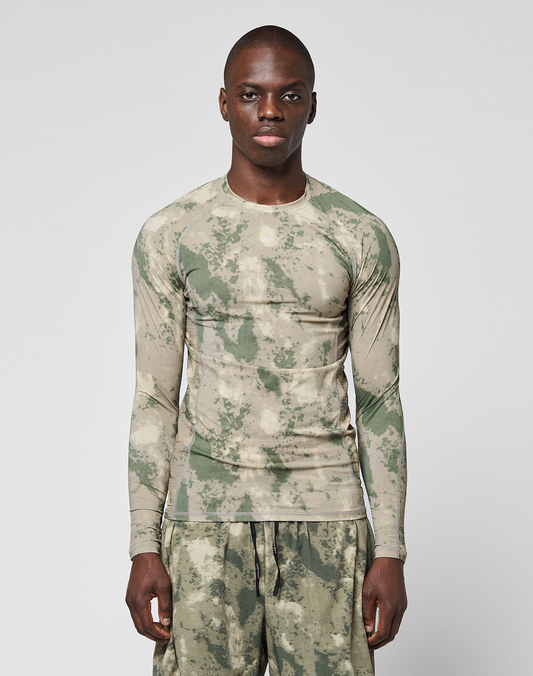 A person wears the LIVE FAST DIE YOUNG LFDY Performance Slim Longsleeve and matching shorts in green and beige camouflage with leichtes Obermaterial, standing against a plain white background. | model