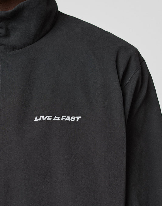 A person wears the LFDY Trackjacket by LIVE FAST DIE YOUNG—a black, oversized jacket with a high collar, white LIVE FAST text and a small running figure graphic on the chest, cropped to show only the upper torso.