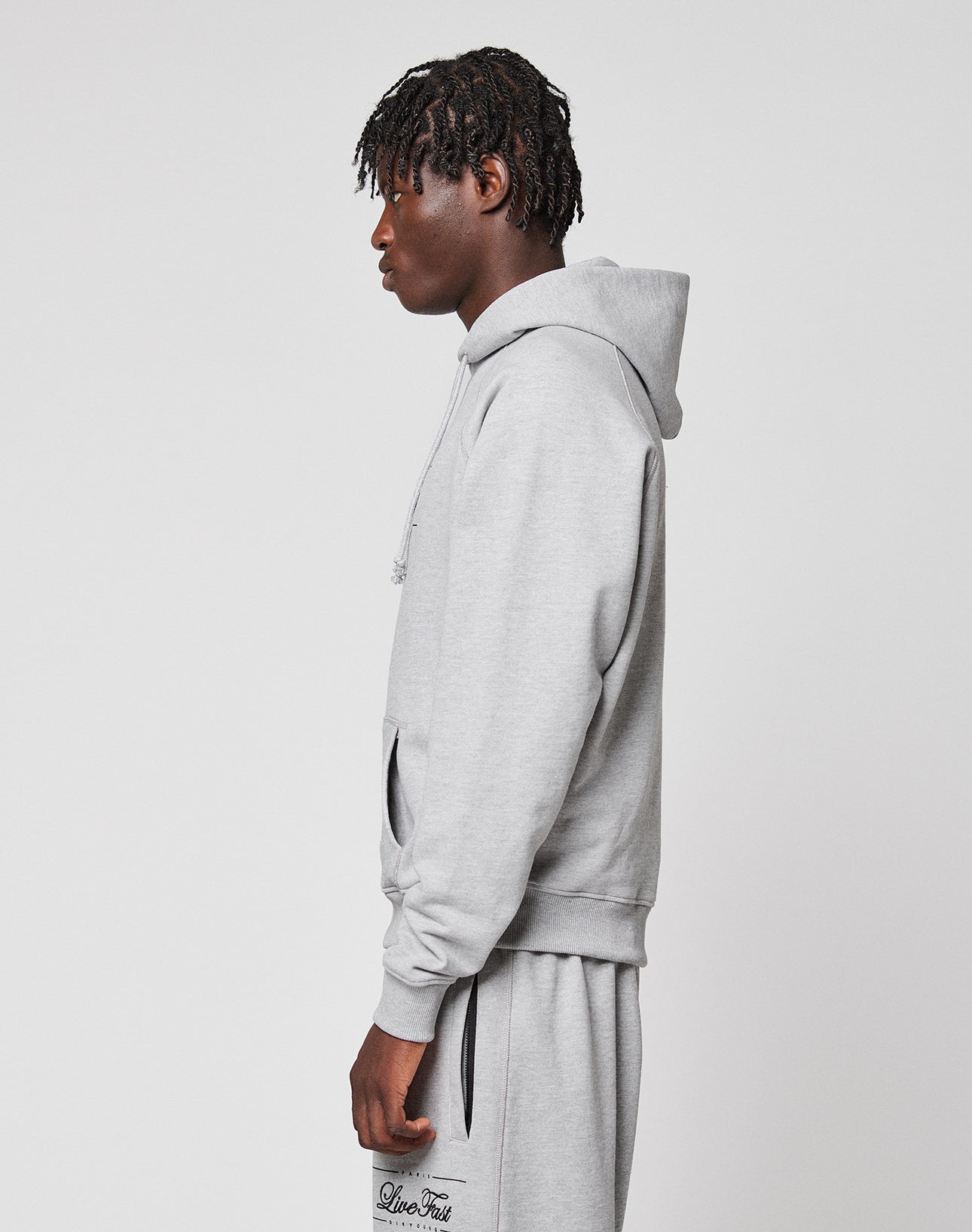 A person with short, textured hair stands sideways in a light gray LIVE FAST DIE YOUNG LFDY Embroidery Hooded and matching sweatpants against a plain white background.