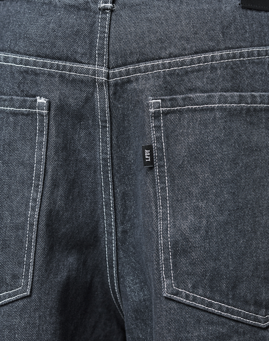Close-up of the back of the LFDY Baggy Denim jeans by LIVE FAST DIE YOUNG, featuring dark gray 100% cotton fabric, two back pockets with white stitching, and a small black tag on the right pocket.