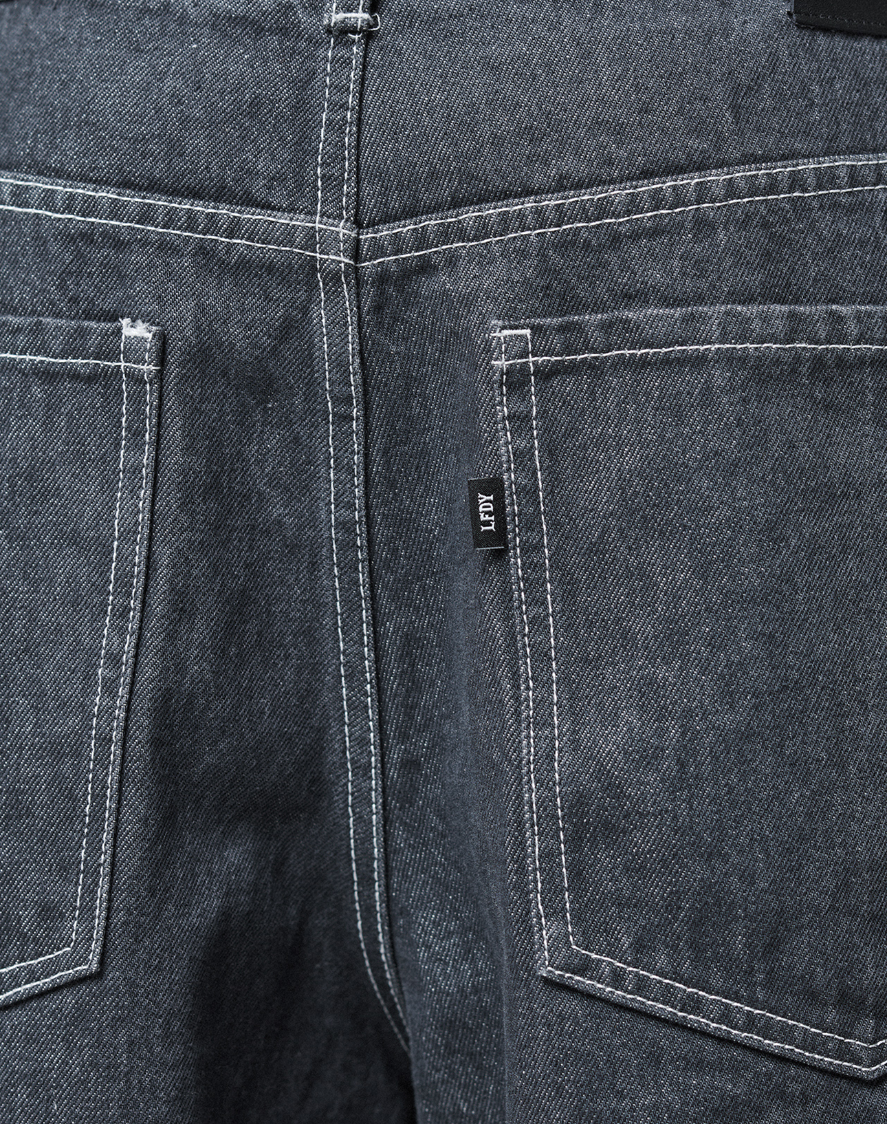 Close-up of the back of the LFDY Baggy Denim jeans by LIVE FAST DIE YOUNG, featuring dark gray 100% cotton fabric, two back pockets with white stitching, and a small black tag on the right pocket.