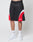A person in LIVE FAST DIE YOUNG Basic Trackshorts—black polyester with white and red curved accents—paired with white LEDY socks and white sneakers, stands against a plain light background. The modern shorts have an oversize fit; upper body not visible.