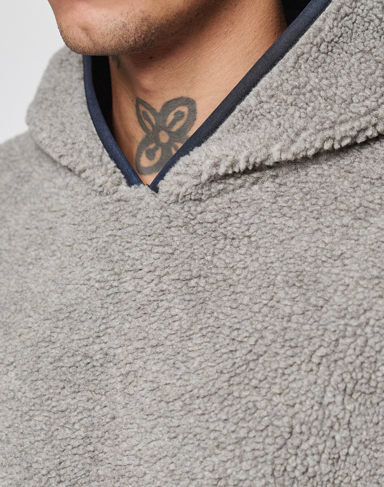 Close-up of a person in the LFDY Teddy Hooded by LIVE FAST DIE YOUNG, a light grey textured fleece hoodie with an oversize fit. Only the lower face and neck with a black and grey floral tattoo are partially visible.