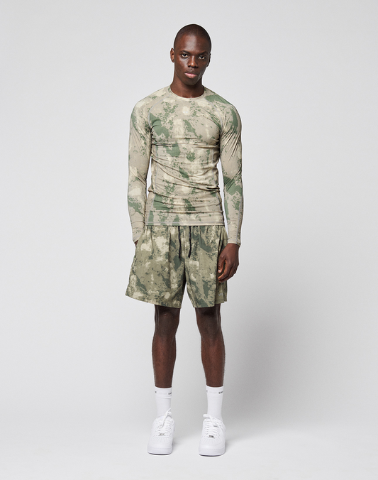 A man stands against a white background wearing a camouflage long-sleeve shirt with reflective logo print, LFDY Performance Running Shorts by LIVE FAST DIE YOUNG, white crew socks, and white sneakers.