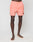A person with dark skin stands barefoot on a white background, wearing LIVE FAST DIE YOUNGs Live Fast Swim Shorts in light coral pink with an elastic waistband, drawstring, and a small circular patch near the left hem. Upper body not visible.