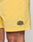 Close-up of a person wearing Live Fast Swim Shorts by LIVE FAST DIE YOUNG in Tinted Yellow Wash. These Regular Fit shorts feature a LIVE FAST patch near the hem and reveal part of the wearer’s thigh.