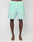 A person stands barefoot on a white surface, wearing mint green LIVE FAST DIE YOUNG Beach Shorts. The image is cropped from the waist to the feet.