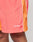 Close-up of a person wearing LIVE FAST DIE YOUNG Beach Shorts in orange and coral with white piping. Features a wide elastic waistband, zippered side pockets, and Live Fast embroidered in white on the left leg.