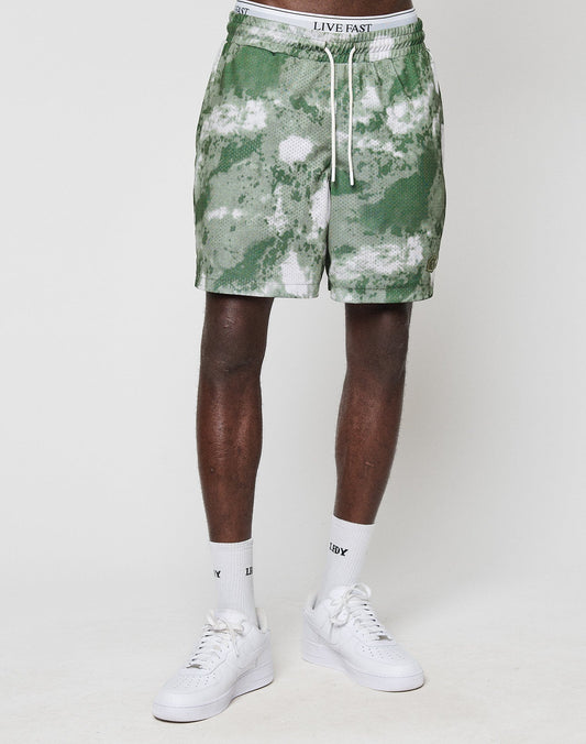 A person wearing green and white LFDY Mesh Shorts by LIVE FAST DIE YOUNG, featuring a LIVE FAST elastic waistband and drawstring, paired with white socks and sneakers, stands against a plain white background. The shorts are soft polyester.