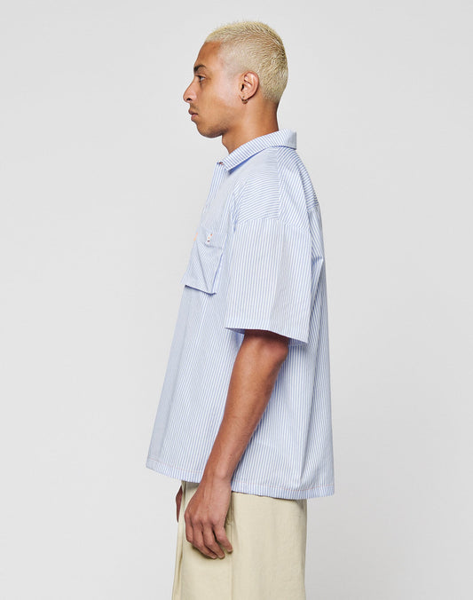 A person with short, bleached blond hair is shown in profile, wearing the LIVE FAST DIE YOUNG LFDY Striped Boxy Shirt in light blue and white stripes and light beige pants, standing against a plain light gray background.