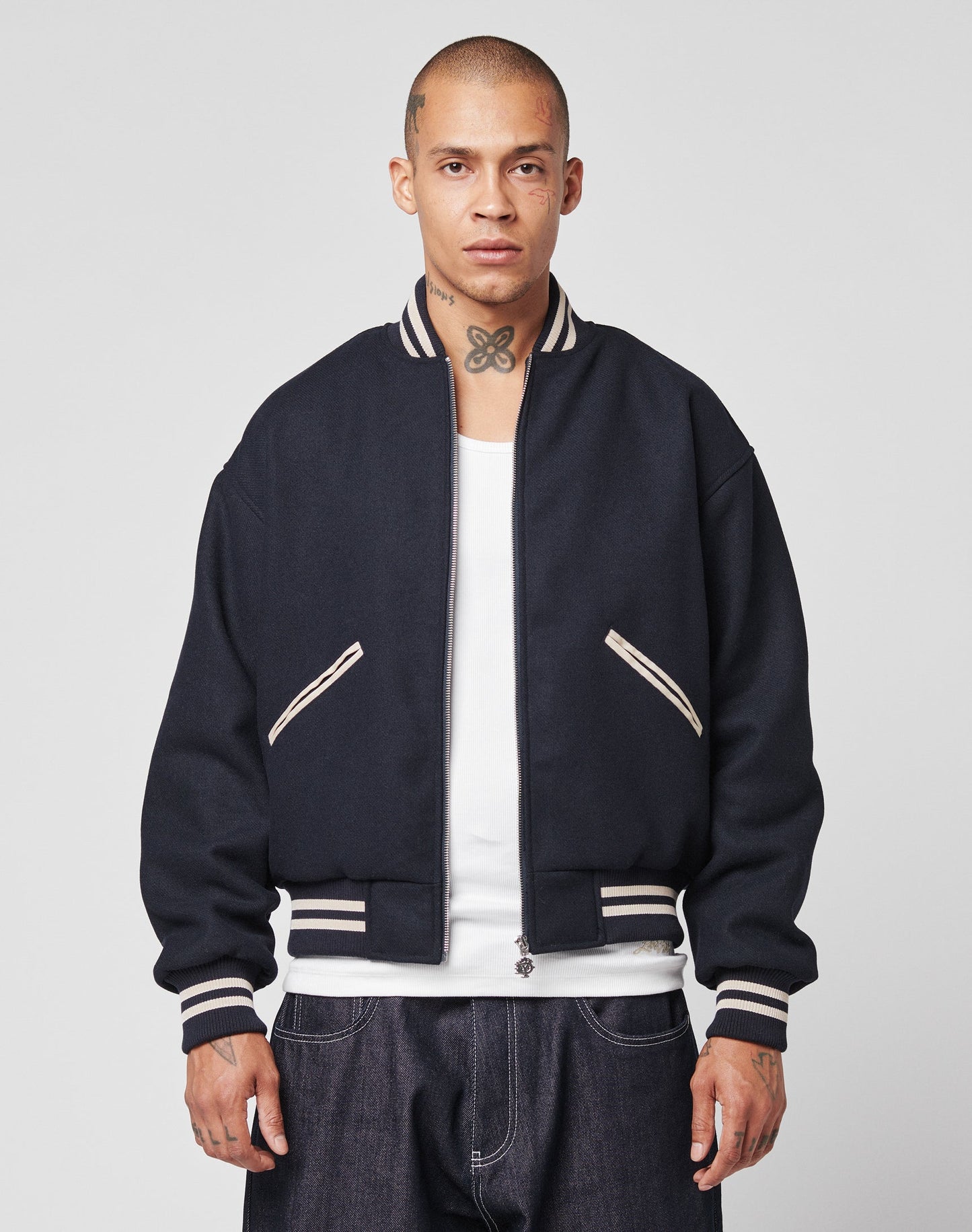 A man with a shaved head and neck tattoo wears the LIVE FAST DIE YOUNG Live Fast College Jacket, a Regular Fit varsity style with DY-Reißverschluss Puller and white trim over a white shirt, facing forward against a plain background.