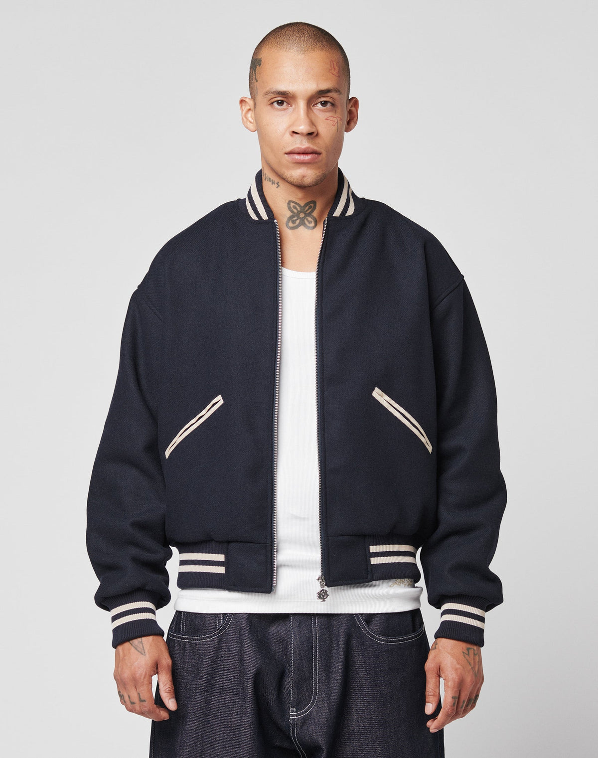 A man with a shaved head and neck tattoo wears the LIVE FAST DIE YOUNG Live Fast College Jacket, a Regular Fit varsity style with DY-Reißverschluss Puller and white trim over a white shirt, facing forward against a plain background.