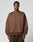 A man with short curly hair and a neutral expression wears the oversize LFDY Wavy Sweater by LIVE FAST DIE YOUNG—a brown Baumwolle-Polyester blend sweatshirt with stitched curves and LIVE IN FAST on the chest. Plain light gray background.