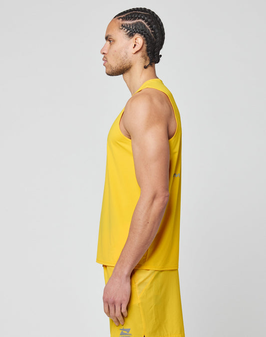 A man with braided hair stands in profile, wearing a slim fit, sleeveless yellow Live Fast Performance Tank and matching yellow shorts by LIVE FAST DIE YOUNG against a plain light gray background.