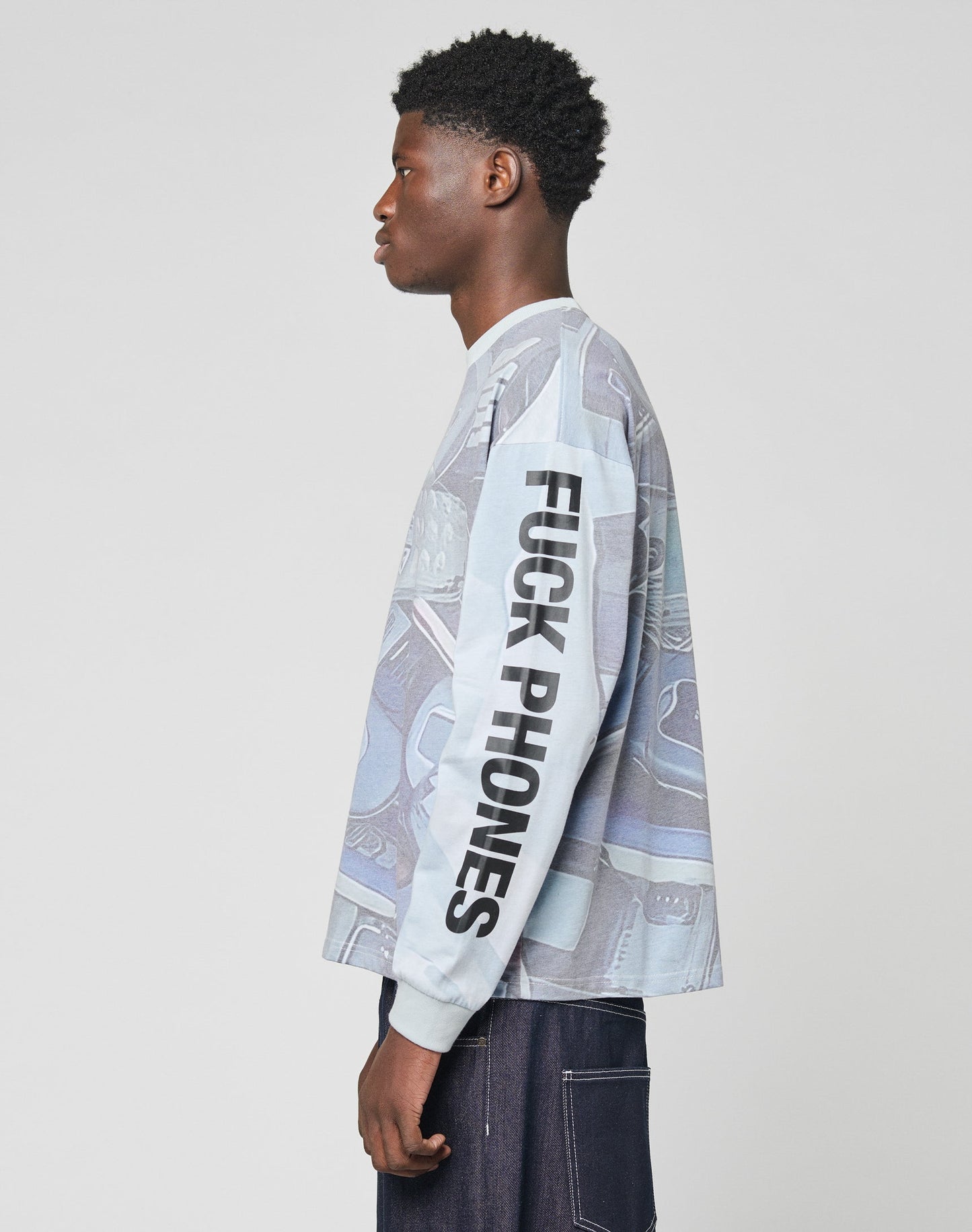 A person in profile wears the LFDY Stolen Phones Longsleeve by LIVE FAST DIE YOUNG, featuring a blue and gray pattern, bold topstitching, an oversized fit, and black “FUCK PHONES” text on the sleeve. The background is plain light gray.