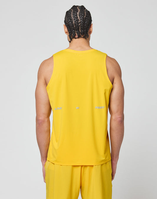 A person with braided hair faces away, wearing the LIVE FAST DIE YOUNG Live Fast Performance Tank in slim fit yellow, paired with matching shorts. LIVE, FAST, and EZ appear as a faint reflective print on the back.