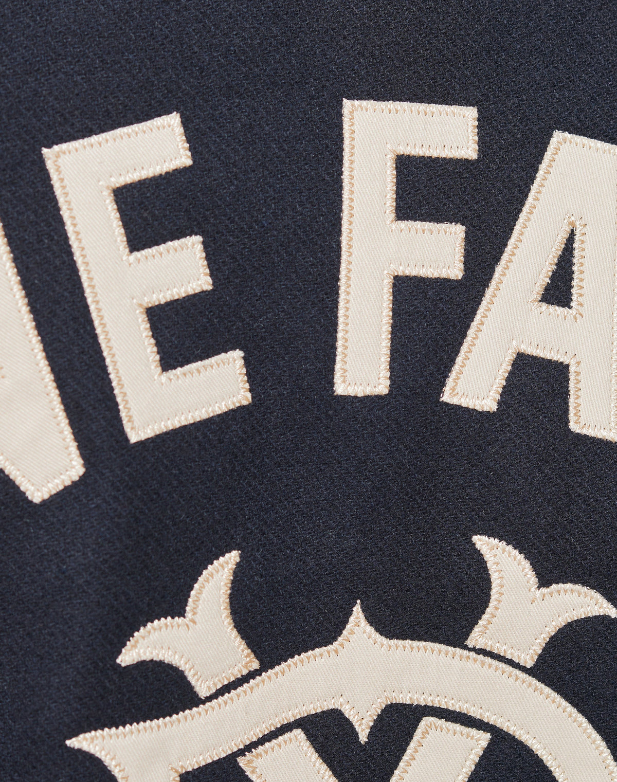 Close-up of cream-colored stitched E and F letters with Rückenstick detail and ornate design on dark fabric, likely from the Live Fast College Jacket by LIVE FAST DIE YOUNG.