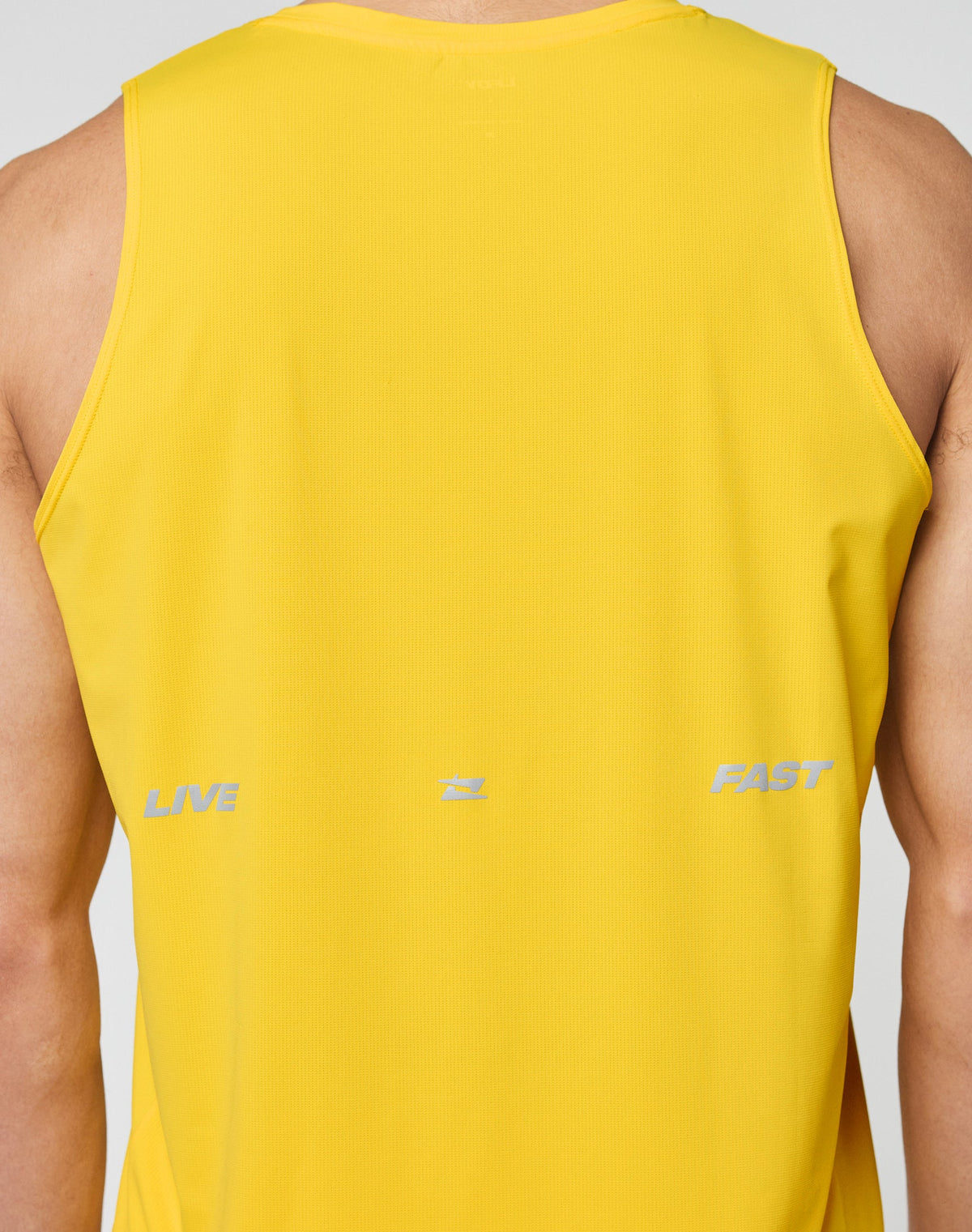 A person wearing the LIVE FAST DIE YOUNG Live Fast Performance Tank—a slim fit, sleeveless yellow nylon-spandex athletic shirt—shown from the back with LIVE and FAST in light gray and a subtle reflective print.