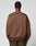 A person with short curly hair is seen from the back, wearing the LIVE FAST DIE YOUNG LFDY Wavy Sweater in oversized brown Baumwolle-Polyester blend, with curved seam details and distressed brown pants, set against a plain light background.