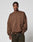 A man stands against a light gray background, wearing the LFDY Wavy Sweater by LIVE FAST DIE YOUNG—an oversized brown sweatshirt with subtle stitching, “LIVE IN PART” on the chest, and paired with dark jeans.