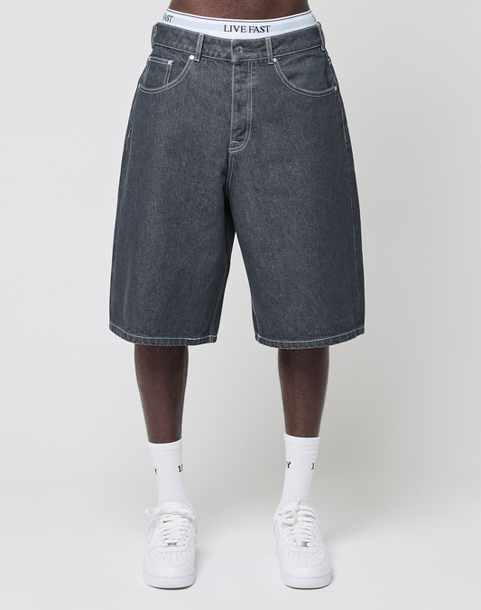 A person stands against a light background wearing LIVE FAST DIE YOUNG's LFDY Jorts in a baggy fit with a visible lederpatch, paired with white socks, white sneakers, and LIVE FAST waistband underwear.