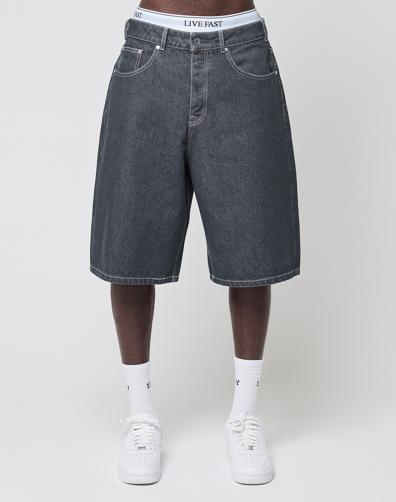 A person stands against a light background wearing LIVE FAST DIE YOUNG's LFDY Jorts in a baggy fit with a visible lederpatch, paired with white socks, white sneakers, and LIVE FAST waistband underwear.
