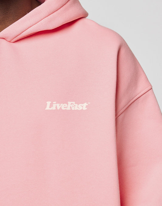 Close-up of a person wearing the LIVE FAST DIE YOUNG Basic 360 Hooded in light pink, featuring white LiveFast text on the left chest, topstitching details, and an oversize fit. Set against a plain, neutral background.