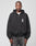Against a plain light gray background, a person wears the LIVE FAST DIE YOUNG Live Fast Lenox Hooded Zip—an oversize fit black zip-up hoodie with LIVE FAST in white on the chest—paired with faded black jeans. Hands at sides, they have a neutral expression.