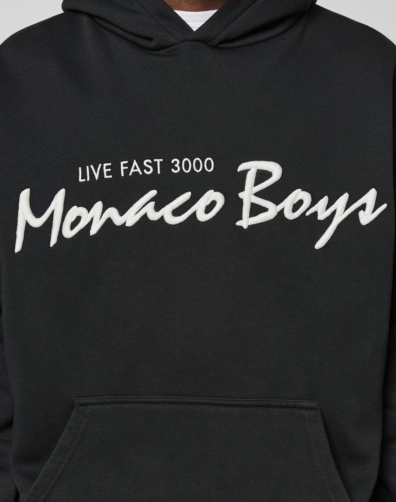 A person is wearing the LIVE FAST DIE YOUNG Monaco Boys Hooded black hoodie with white 3D Stick text. Made from a comfy Baumwolle-Polyester Mix, only the torso and part of the oversize-fit hood are visible.