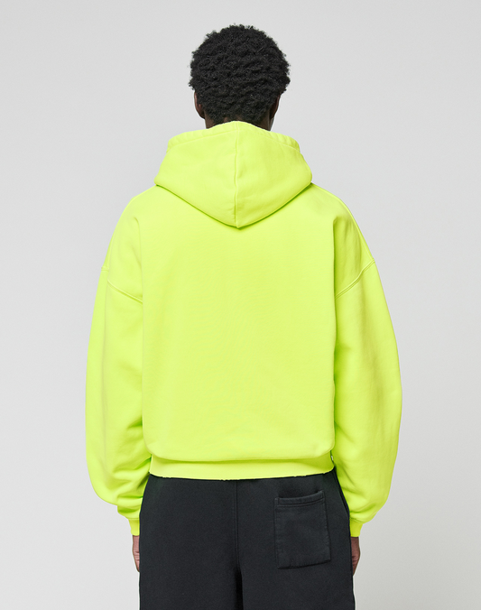 A person faces away from the camera, wearing an oversize fit LIVE FAST DIE YOUNG Basic Hooded Zip in bright yellow and black pants with a back pocket, set against a plain light gray background.