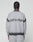 A person with braided hair, seen from behind, wears the LIVE FAST DIE YOUNG Live Fast Boucle Sweater in light gray. "LIVE FAST" and a bird graphic are on the back with a faded spray effect and dark gray stripes at shoulders and hem.
