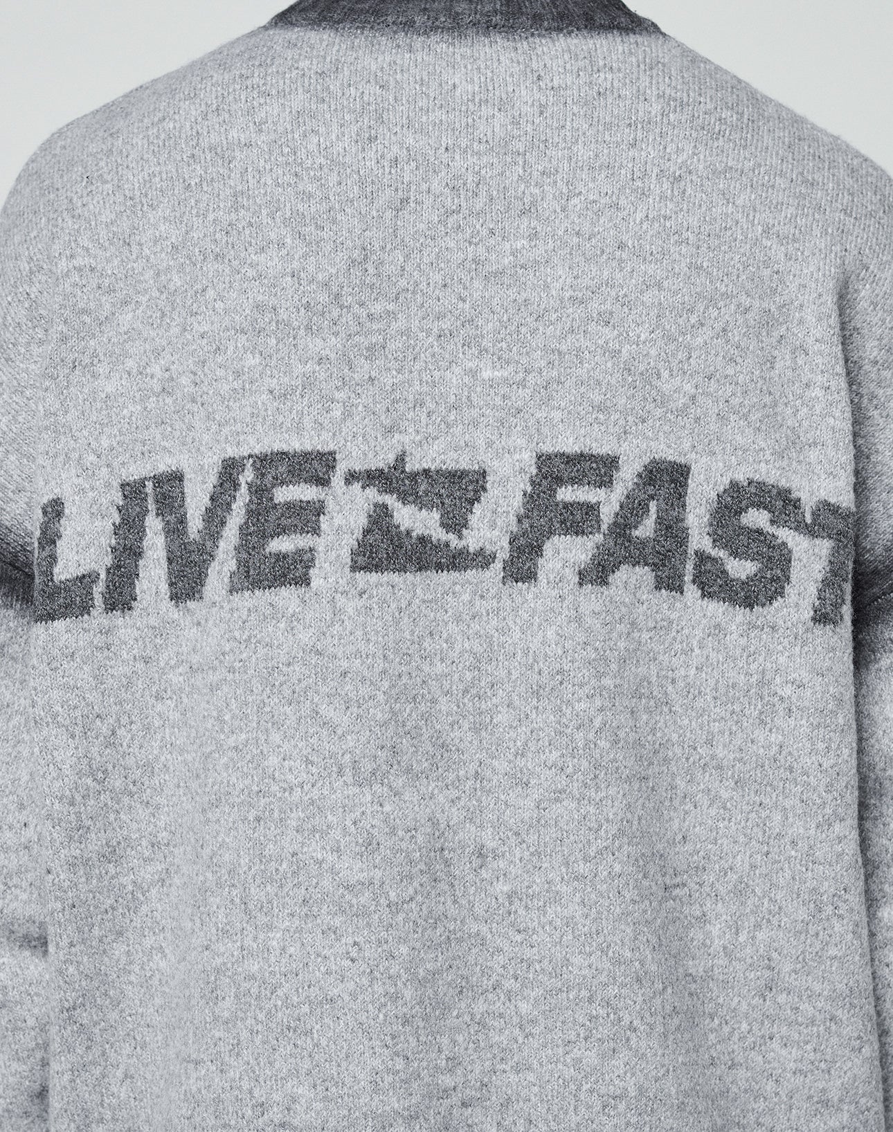 Back of a gray Live Fast Boucle Sweater by LIVE FAST DIE YOUNG, featuring "LIVE FAST" in bold print with the A as a running figure and a faded spray effect. Oversize fit adds comfort.