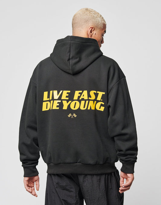 A person with short blond hair is wearing the LIVE FAST DIE YOUNG LFDY Drift Hooded sweatshirt, featuring yellow “LIVE FAST. DIE YOUNG.” text on the back, a doppellagige Kapuze, and a comfy cotton-polyester blend.
