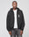 A person wears a LIVE FAST DIE YOUNG Live Fast Lenox Hooded Zip, a black oversize fit zip-up hoodie with front and back print, over a white t-shirt and gray jeans, standing against a plain light gray background with a neutral expression.