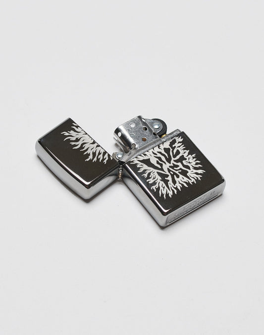 The LFDY x Zippo by LIVE FAST DIE YOUNG is a metal flip-top lighter with a black aluminum case and an intricate white tree or lightning design, making it a limited edition collector’s item.