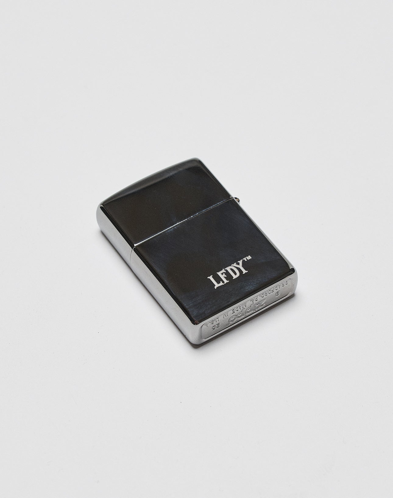 A sleek, black and silver LFDY x Zippo by LIVE FAST DIE YOUNG with an Aluminium-Gehäuse and LFDY branding on the front, displayed on a plain white background.