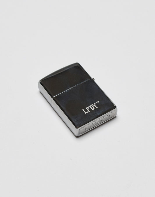 A sleek, black and silver LFDY x Zippo by LIVE FAST DIE YOUNG with an Aluminium-Gehäuse and LFDY branding on the front, displayed on a plain white background.
