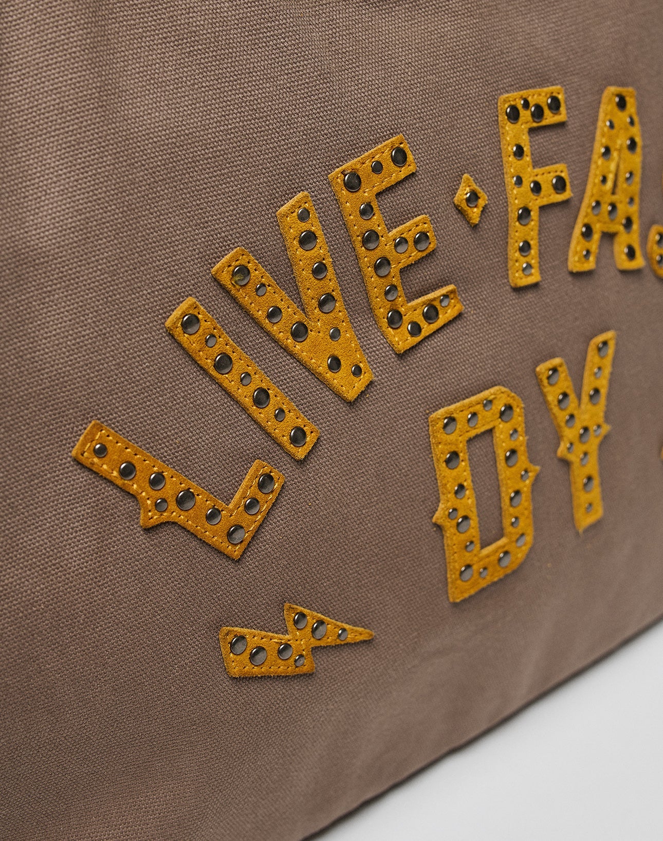 The LFDY Tote Bag by LIVE FAST DIE YOUNG features brown fabric, yellow studded LIVE ● FA... DY text, a lightning bolt design, Rindsleder accents for durability, and a dedicated laptop compartment.