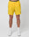 Someone stands against a white background wearing LIVE FAST DIE YOUNG’s bright yellow Live Fast Performance Shorts with a black waistband that reads LIVE FAST, paired with white socks and white sneakers.