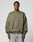 A man in the LFDY Wavy Sweater by LIVE FAST DIE YOUNG, an oversized olive green cotton-poly blend with subtle curved seams and light chest text, pairs it with wide-leg light jeans while standing against a plain gray background.
