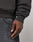 A close-up of a person’s hand resting by their side, wearing the LIVE FAST DIE YOUNG Live Fast Stallion Hooded sweatshirt and faded black jeans with a visible front pocket against a plain, light-colored background.