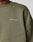 Close-up of a person wearing the LFDY Wavy Sweater by LIVE FAST DIE YOUNG, an olive green oversize fit with LIVE FAST in white on the chest. Made from a soft Baumwolle blend, it has visible stitching and a ribbed neckline.