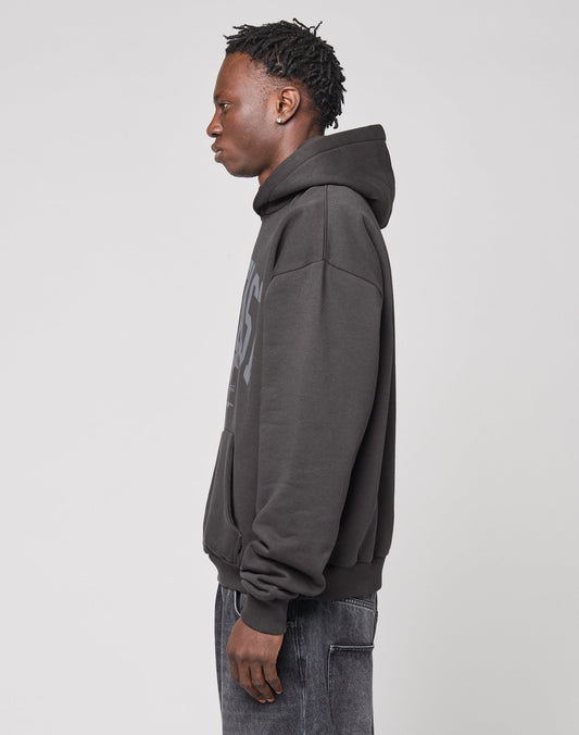 A person with short, textured hair stands in profile against a plain background, wearing the LIVE FAST DIE YOUNG Live Fast Stallion Hooded—a dark, oversized hoodie crafted from soft Baumwolle with an eye-catching front print—and dark jeans.