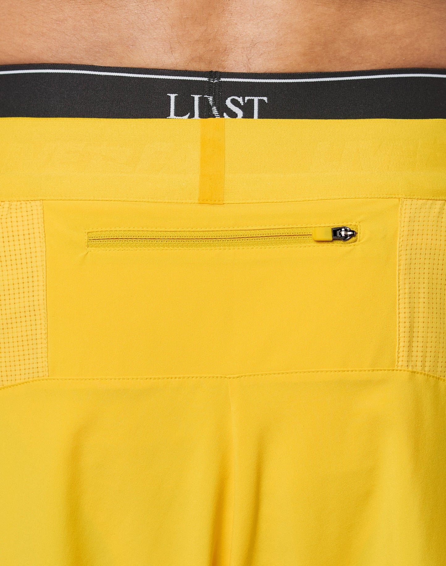 Close-up of the back of bright yellow Live Fast Performance Shorts by LIVE FAST DIE YOUNG, featuring a small zippered pocket and an Elastikbund waistband with black LIVST underwear partially visible above.