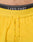 Close-up of a person’s lower torso wearing LIVE FAST DIE YOUNG’s bright yellow Live Fast Performance Shorts with a drawstring, paired with black underwear featuring the words LIVE FAST on the waistband.
