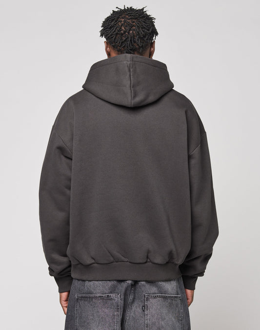 A person stands facing away from the camera, wearing a dark gray LIVE FAST DIE YOUNG Live Fast Stallion Hooded with Oversize Fit and faded gray jeans, set against a plain light background.