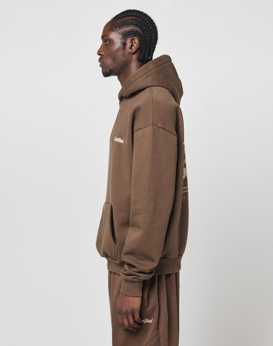 A man with braided hair stands in profile wearing an oversize fit brown LIVE FAST DIE YOUNG Basic 360 Hooded sweatshirt and sweatpants, made from a soft cotton-polyester blend, set against a plain white background.