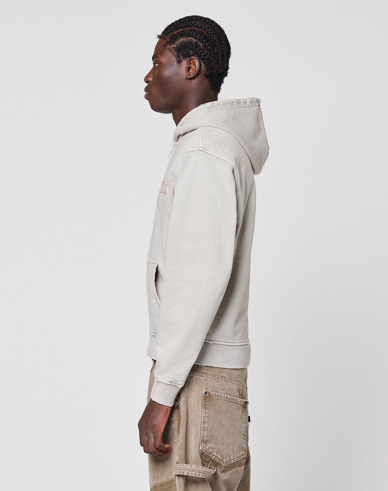 A person with braided hair, dressed in a light gray LFDY Corp. Hooded Zip by LIVE FAST DIE YOUNG and brown cargo pants, stands in profile against a plain white background.
